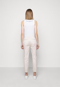 Top sans manches blanc, pantalon tapered beige clair en tissu mélangé coton, vue arrière, sans motifs visibles, associé à des baskets blanches.