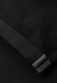 Tissu noir à texture lisse se plie sur lui-même, présentant un bord replié avec un accent gris et des détails de couture subtils.