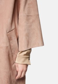 Hellrosa Wildlederjacke mit weiten Ärmeln und sichtbarer Seitentasche. Unter dem Ärmel in Beige befindet sich eine Knopfverzierung an der Manschette.