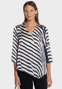 Blouse à rayures bleu marine et blanches avec un col en V, des manches trois-quarts et un ourlet asymétrique, confectionnée dans un tissu lisse et léger.