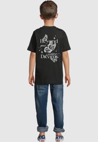 Black t-shirt with a white graphic design of butterflies and the text "Beyond your wildest Dreams" on the back. Casual fit with short sleeves.