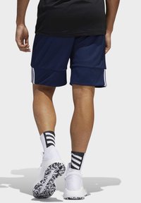 Marineblaue Sportshorts mit weißen Seitenstreifen, kombiniert mit weißen Schuhen und Socken mit schwarzen Streifen, von hinten gesehen und zeigt den glatten Stoff.