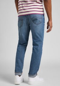 Vaaleansiniset rentot leikatut farkut, joissa on kaksi takataskua ja käännetty helma, yhdistettynä valkoisiin lenkkareihin.