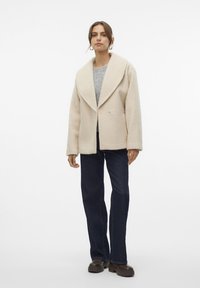 Off-white oversized kappa i ullblandning med breda slag, texturerad yta, framknappar, lagd över en grå tröja och mörka denimjeans.