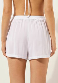 Pantalones cortos blancos de tela ligera, con una cintura elástica y dobladillo doblado. Diseño sencillo sin patrones ni acentos adicionales.