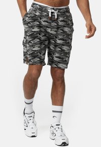 Pantalones cortos cargo de camuflaje gris con cintura elástica, cordón blanco y bolsillos laterales. Llevados con zapatillas blancas y calcetines cortos.