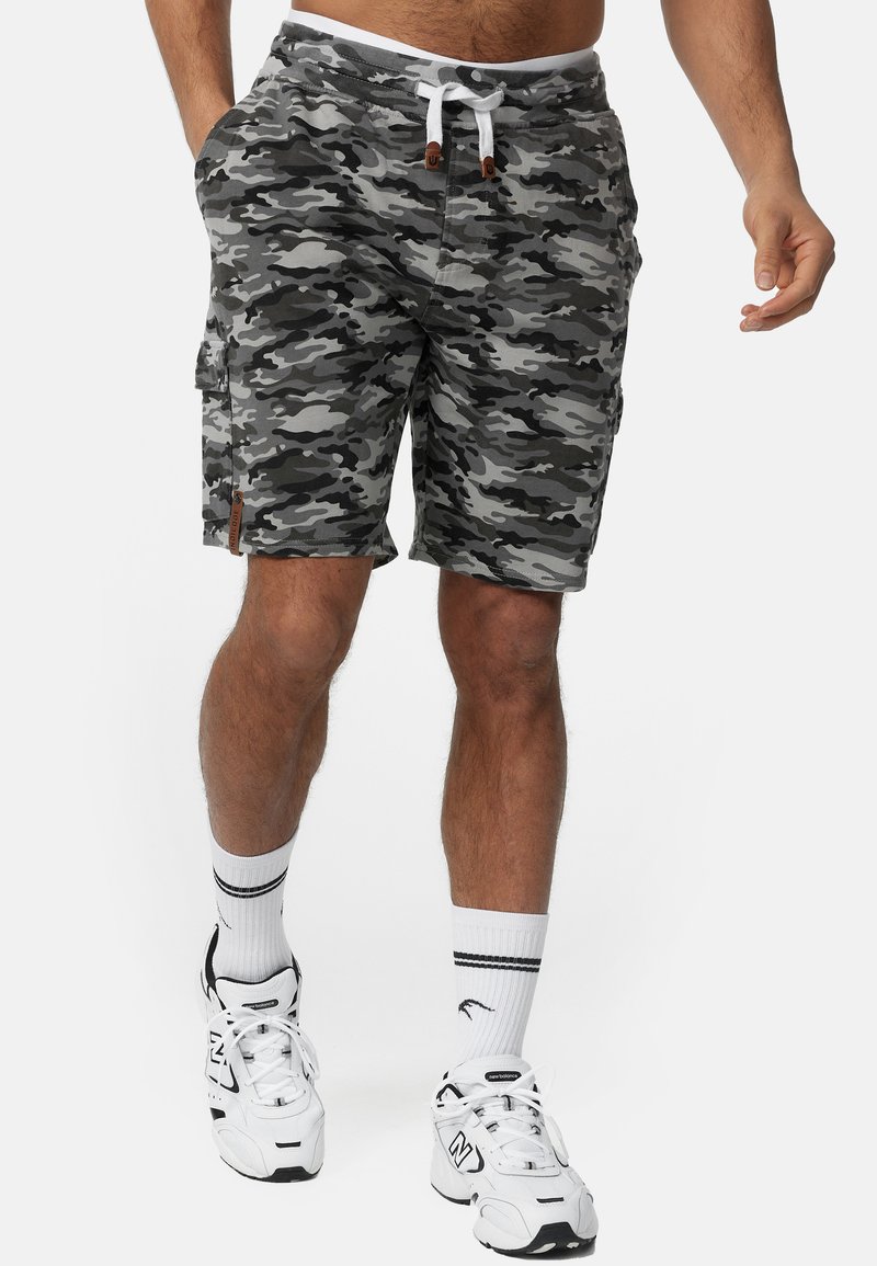 Grå kamouflage cargo shorts med ett elastiskt midjeband, vit dragsko och sidofickor. Bärs med vita sneakers och strumpor.