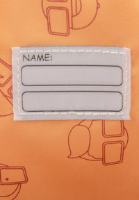 Narancssárga textil, fehér, varrott címkével, amelyen az "NÉV:" felirat szerepel, valamint két sor szöveg számára. A háttérben halvány, ismétlődő illusztrációk találhatók.