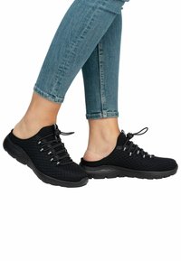 Scarpe slip-on nere in mesh con superficie texturizzata, lacci elastici e suola in gomma spessa, mostrate insieme a jeans skinny in denim blu.