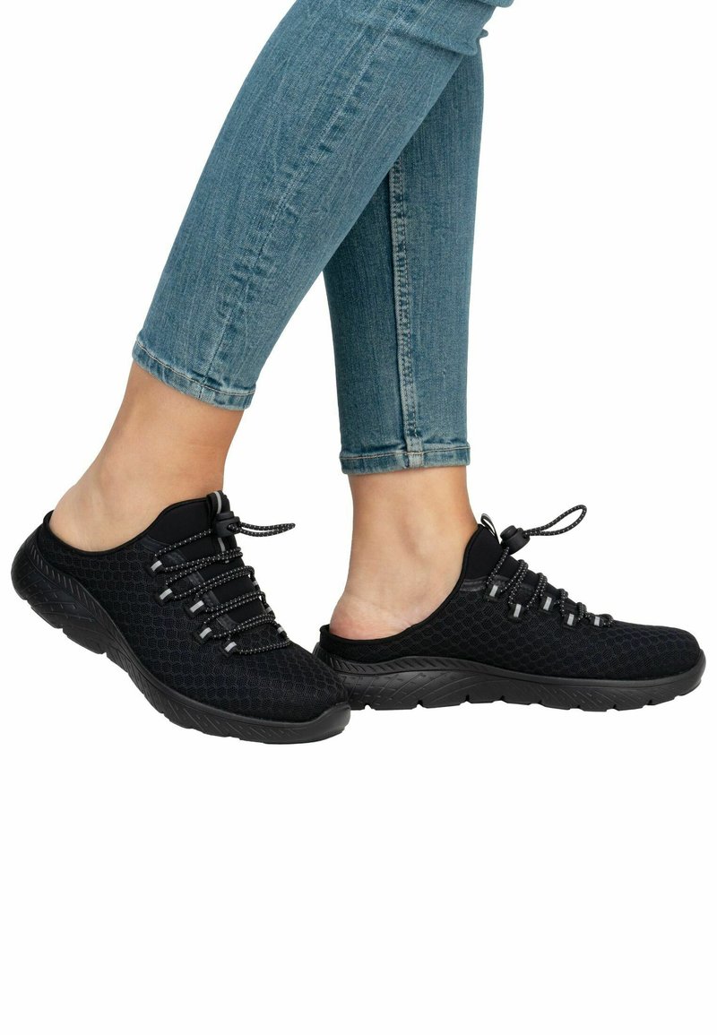 Scarpe slip-on nere in mesh con superficie texturizzata, lacci elastici e suola in gomma spessa, mostrate insieme a jeans skinny in denim blu.