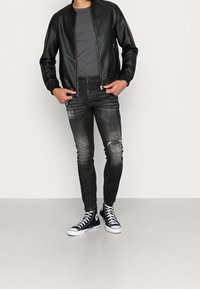 Czarna skórzana kurtka typu bomber noszona na szarej koszulce, zestawiona z dopasowanymi czarnymi dżinsami z przetarciami i czarnymi wysokimi trampkami.