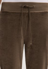 Bruine velours sweatpants met een elastische tailleband en koord. Zachte textuur, elastische band en een gladde afwerking. Close-up van de tailleband en de stofdetails.