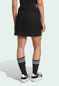 Černá džínová sukně s elastickým pasem, vybavená zadními kapsami a bočními pruhy. Kombinována s černými podkolenkami a sneakers.