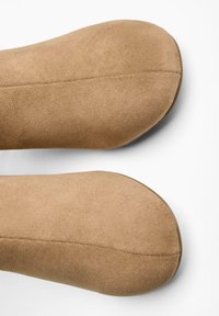 Încălțăminte din suedin bej cu vârf rotund și textură netedă. Prezintă o cusătură subtilă și talpă plată, potrivită pentru ținute casual.