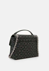 Sort og grå Calvin Klein håndtaske med gentagne "ck" logo mønster, top håndtag og sølv kæde skulderrem mod hvid baggrund.