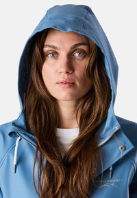 Giacca impermeabile blu con cappuccio, caratterizzata da una zip anteriore, dettagli con cordino e logo. Texture liscia con un design elegante.