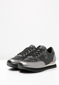 Svarta och grå sneakers med en texturerad tygöverdel, metalliska detaljer, snörning och en gummisula med ett mönster av småridgar.