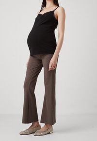 Svart cami-top med spetsdetaljer, bruna randiga utsvängda byxor och dekorerade platta skor med metalliska accenter. Modellen är gravid.