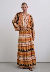 Conjunto multicolorido que presenta una blusa corta y estampada y una falda larga con volantes en diseños geométricos en naranja, negro y blanco.