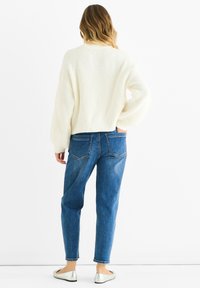 Maglione bianco a coste e jeans blu a vita alta. Il modello indossa ballerine argentate. Il maglione ha una vestibilità comoda, con maniche a palloncino.