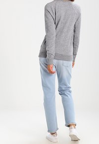 Grijze trui met geribbelde manchetten en zoom, gecombineerd met lichtblauwe spijkerbroek en witte sneakers, gezien van achteren.