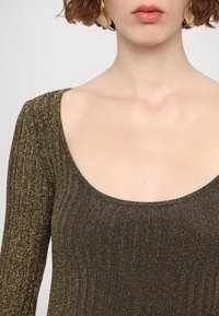 Top marrone in maglia a coste con scollo rotondo. Il tessuto ha una finitura metallica, aggiungendo texture e interesse visivo.