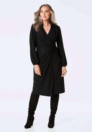 Robe noire cintrée à manches longues, avec un détail de taille froncée et une texture lisse, associée à des bottes noires à talons montant jusqu'aux genoux.
