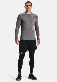 Grå langermet treningsskjorte, svarte shorts og svarte leggings. Skjorten har et lett teksturert stoff, med Under Armour-logo detaljer.