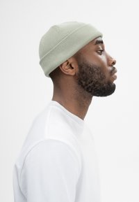 Lichtgroene gebreide muts met ribbeltextuur, gedragen door een persoon met een korte baard, gecombineerd met een witte crewneck t-shirt.