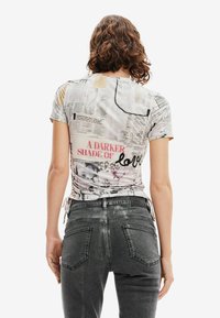 Camiseta ajustada de manga corta con un diseño de medios mixtos, que presenta texto e imágenes en tonos de beige, blanco y negro. Vista trasera.
