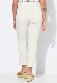 Béžové zkrácené kalhoty s přiléhavým střihem, se zadními kapsami a vyšitými detaily na nohavicích. Nosené s platformovými sandály.