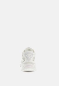 Chaussure de sport blanche avec une tige en mesh, un collier rembourré et une semelle épaisse et translucide. Présente un logo triangulaire texturé au niveau du talon.