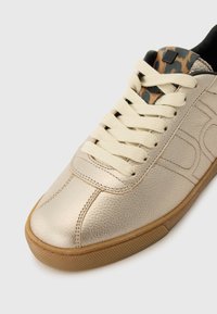 Sneaker dorato metallizzato con tomaia in pelle testurizzata, lacci crema e fodera con stampa leopardata. Presenta una suola in gomma con grip testurizzato.