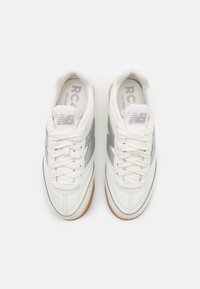 Une paire de baskets blanches New Balance avec des logos gris clair et des semelles en gomme, présentée de dessus sur un fond blanc.