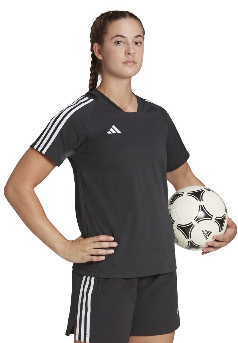 Maillot de soccer noir avec des rayures blanches sur les manches, associé à un short noir. Tenant un ballon de soccer blanc avec des accents noirs.