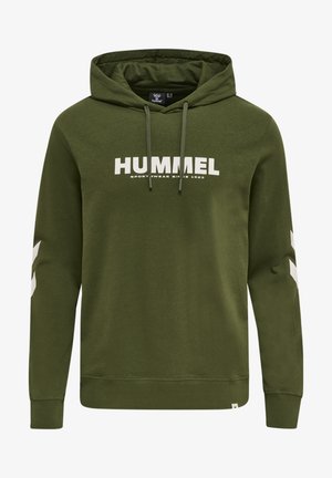 Frau trägt olivgrünen Hummel-Hoodie und passende Hose mit weißen Chevron-Logos auf den Ärmeln und dem Schriftzug "HUMMEL" auf der Brust.