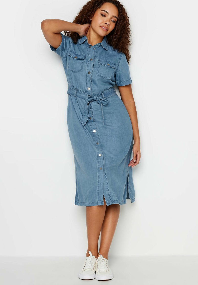 Denim mekko vaaleansinisessä, polvimittainen, lyhythihainen, jossa on kaksi rintataskua ja vyötäröllä solmittava vyö. Napitus edessä ja sivuventtiilit.