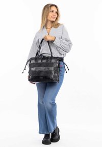 Zwarte handtas met een gestructureerd, patroonoppervlak; dubbele handgrepen; trekkoordsluiting; gecombineerd met blauwe flared jeans en zwarte enkellaarsjes.