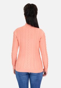 Suéter de punto color coral claro con patrón de trenzas, mangas largas, diseño ajustado y dobladillo acanalado. Llevado con jeans de mezclilla azules.