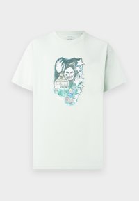 Ανοιχτό πράσινο βαμβακερό t-shirt με γραφικό σχέδιο που απεικονίζει ένα κρανίο, ένα σπίτι και αστέρια. Λαιμόκοψη crew, κοντά μανίκια και άνετη εφαρμογή.