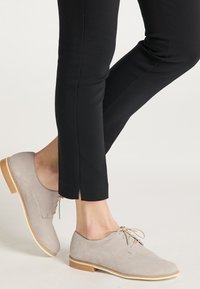 Lichtgrijze suède schoenen met een ronde neus, platte houten hak en ton-sur-ton veters, gecombineerd met zwarte slim-fit broek met een split aan de onderkant.