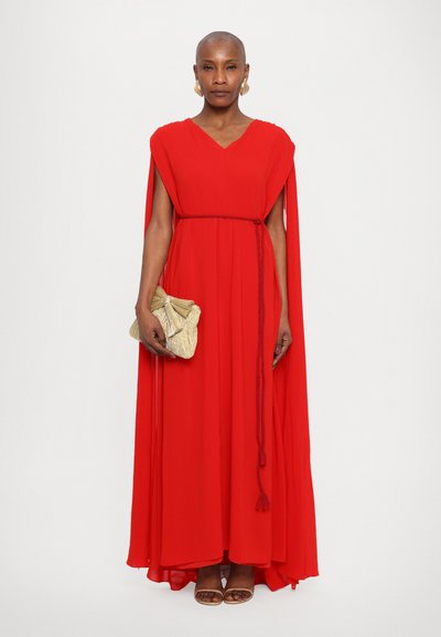 Red maxi dress with a v-neck, cape sleeves, and a waist tie. Features a textured, metallic clutch and simple tan sandals.