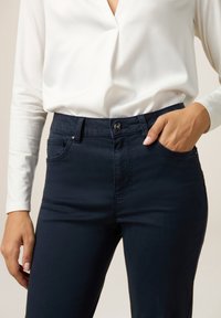 Marineblauwe slimfit broek met een gladde textuur, voorzien van een knoop- en ritssluiting, voorzakken en versterkte naden.