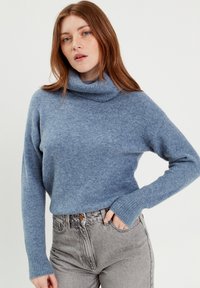 Light blue turtleneck sweater made of soft material, featuring ribbed cuffs, relaxed fit, and slightly textured surface, paired with gray jeans.