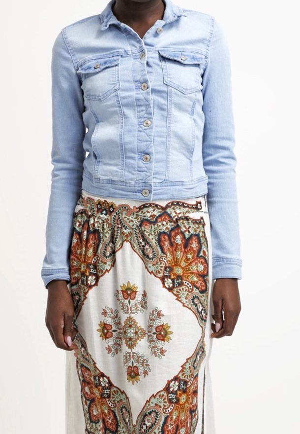 Light blue denim jacket with two front pockets, button closure, and long sleeves, worn over a patterned, flowy skirt featuring floral designs.