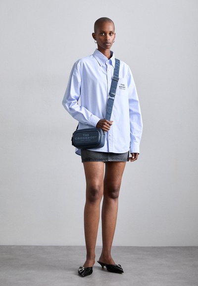 Cămașă albastră cu dungi și mâneci lungi, fustă din denim gri și balerini negri ascuțiți. Geanta tip crossbody este confecționată din material albastru închis, cu text embosat.