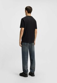 Zwarte korte mouwen t-shirt van katoen, gecombineerd met vervaagde blauwe jeans. De outfit heeft een relaxte pasvorm en minimale details.