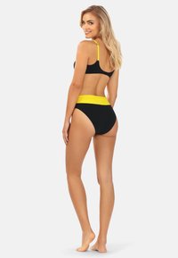 Czarny zestaw bikini z topem bez pleców i żółtymi ramiączkami oraz wysokim stanem z kontrastującą żółtą taśmą. Gładka tekstura.