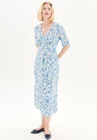 Robe portefeuille fleurie à manches courtes, présentant un motif bleu et vert sur un fond clair. Associée à des ballerines navy.