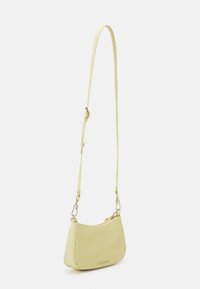 Petit sac bandoulière jaune clair avec bandoulière réglable et fermeture éclair, présenté sur un fond clair uni.